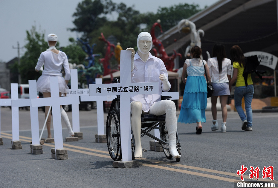4月16日，重慶市洋人街上擺放著兩個受了傷的塑料人像“模特”，旁邊十字架上寫著向“中國式過馬路”說不