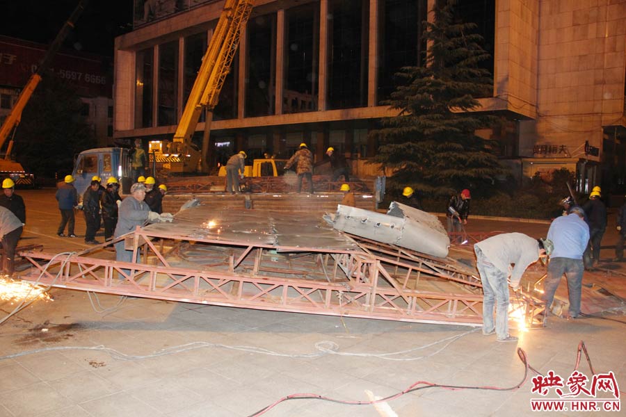 地面上的20多名工人對吊裝下的廣告牌進(jìn)行分割。