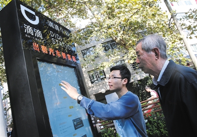 10月15日，滴滴工作人員（左）指導(dǎo)乘客使用“滴滴車站”的電子屏預(yù)約出租車。