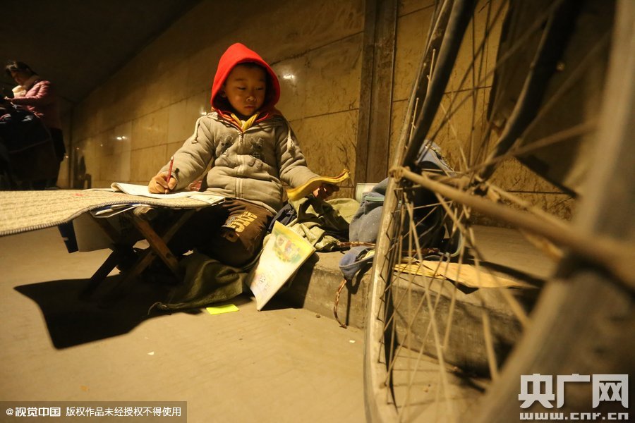 2015年11月8日晚，鄭州，7歲男孩涵洞橋下陪父母練攤，路邊燈下坐小馬扎上寫作業(yè)。