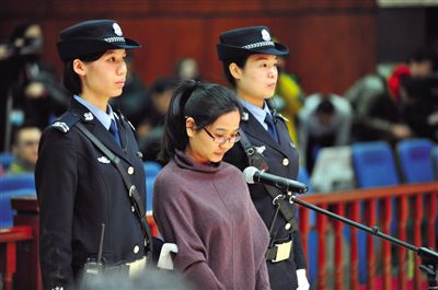 被告人盧梅低著頭，站在朝陽法院刑事審判庭的被告席上。