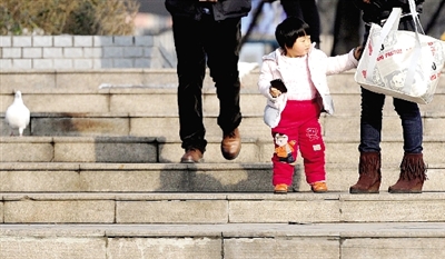 昨天中午，一女孩拉著家長(zhǎng)的手在紫荊山公園曬太陽，氣溫升高，孩子的棉衣解開了扣子。