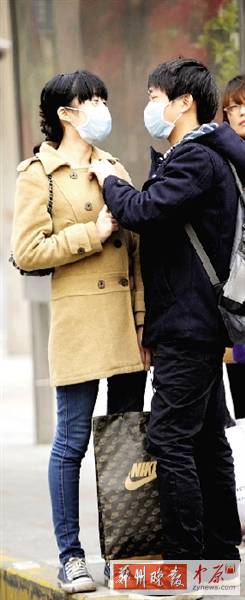 公交站臺(tái)上，一對(duì)年輕人戴著口罩，系緊衣領(lǐng)。